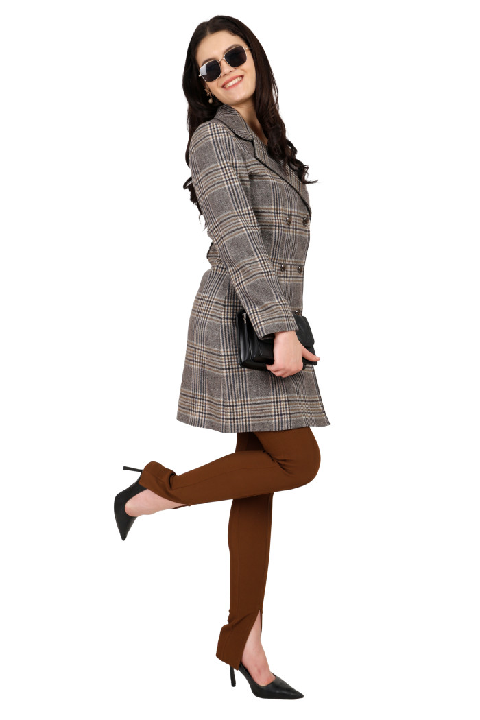 A woman in a standing side pose in black shades, wearing Trufit’s brown double breast woolen tweed long coat with a lapel collar, button closure, side pockets and styled in brown jeans while holding a clutch from her right hand.