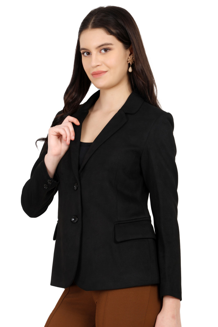 A woman is giving a standing side pose wearing Trufit’s short-length coat in black with a lapel collar, side pockets, and a button closure styled in brown jeans while holding the collar from her right hand.