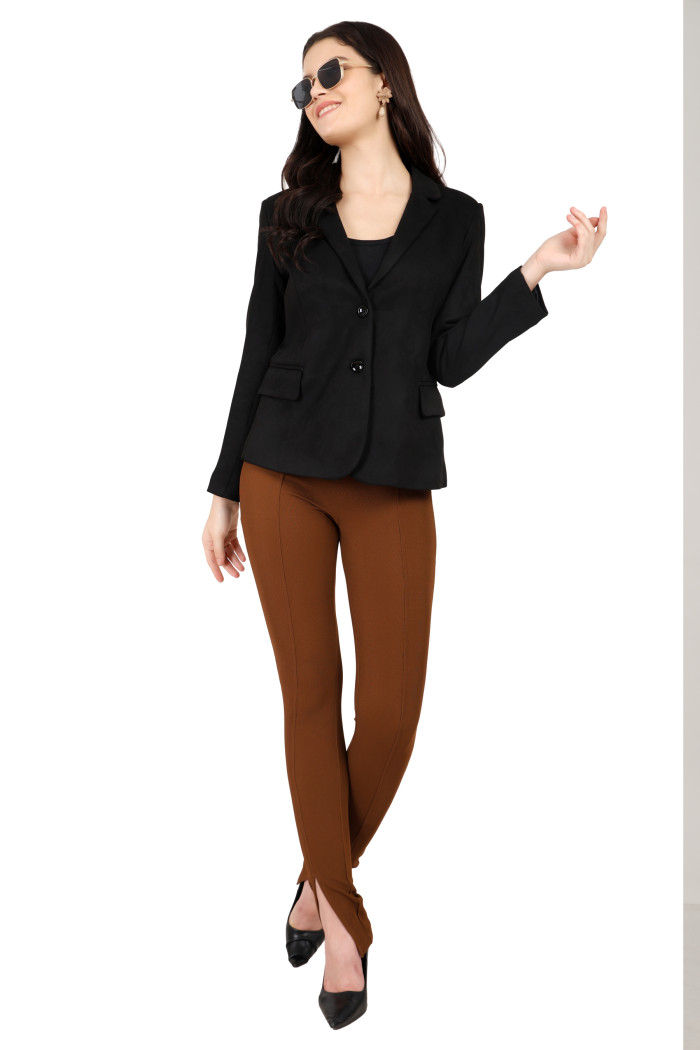 A woman in a standing pose is wearing black shades, Trufit’s short-length black coat with a lapel collar, side pockets, and a button closure styled in brown jeans.