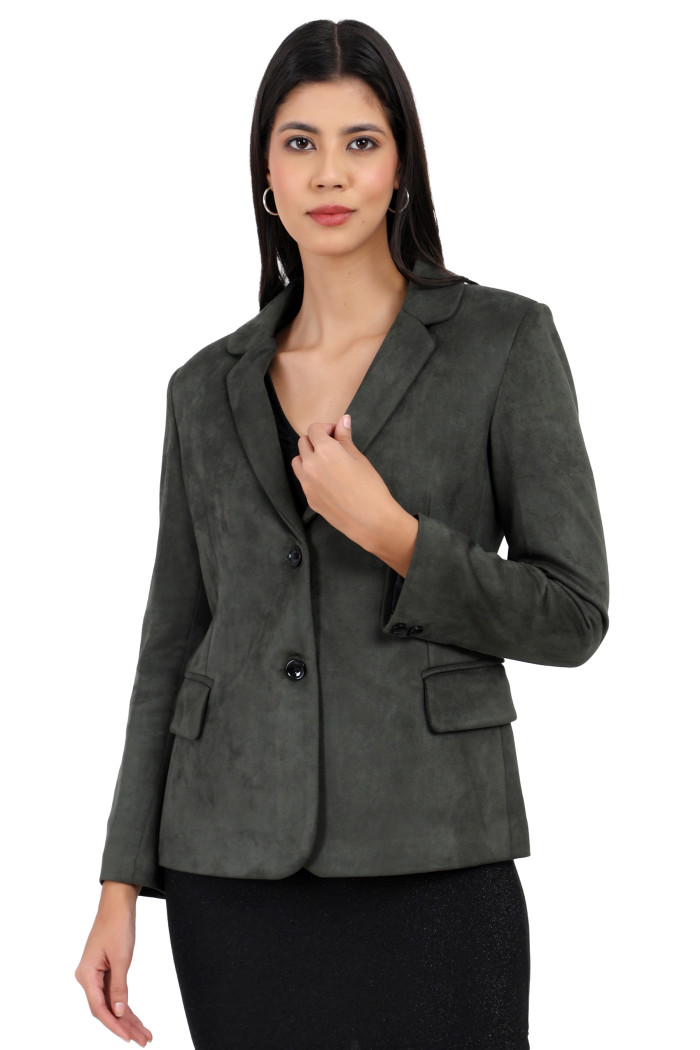 A woman is giving a standing side pose wearing Trufit’s short-length coat in olive with a lapel collar, side pockets, and a button closure in one piece while holding the collar with her left hand.