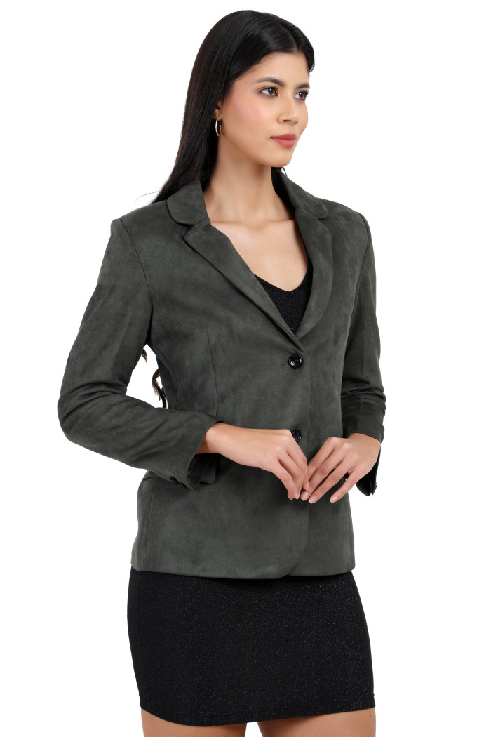 A woman is giving a standing side pose wearing Trufit’s short-length coat in olive with a lapel collar, side pockets, and a button closure in one piece while holding her hands.