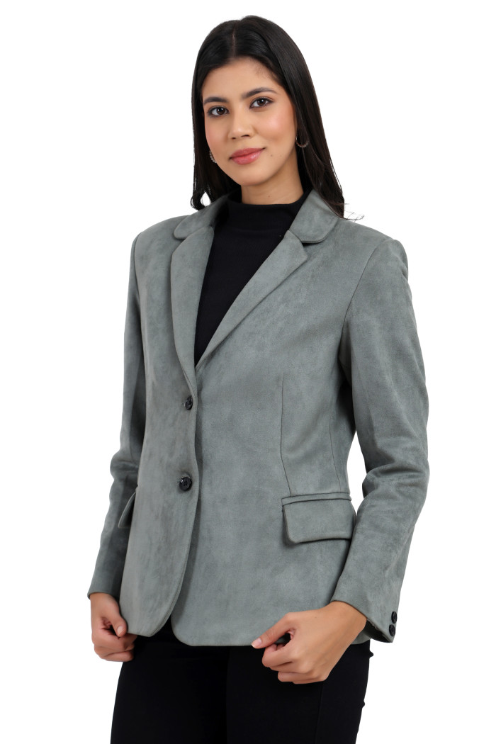 A woman is giving a standing side pose wearing Trufit’s short-length coat in pista with a lapel collar, side pockets, and a button closure in black jeans while holding the coat.