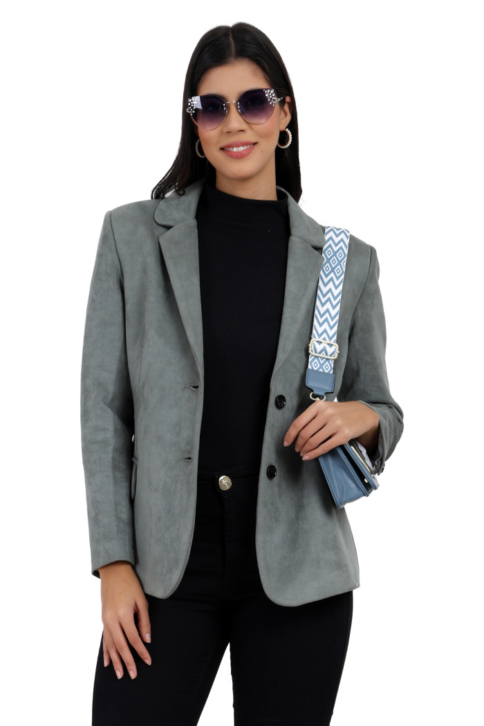 A standing pose of a woman in black shades wearing Trufit’s short-length coat in pista with a lapel collar, side pockets, and a button closure in black jeans while holding a clutch from her right hand.