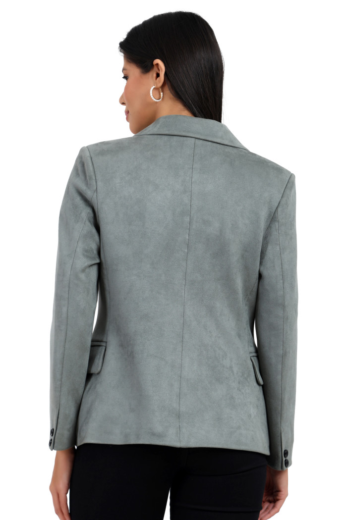 A back pose of a standing woman wearing Trufit’s short-length coat in pista with a lapel collar and black jeans.