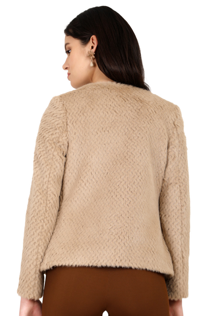 A back pose of a standing woman wearing Coatsnmore’s beige short-length coat and brown jeans.