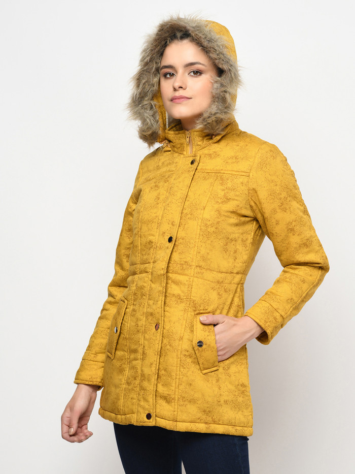 A right pose of a woman wearing a Mustard Puffer jacket with a high neck, hood, zipper closure and side pocket designed for casual winter layering and comfort.