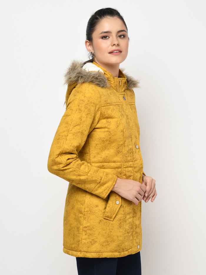 A left pose of a woman wearing a Mustard pufferjacket with a high neck, hood, zipper closure and pocket in hand designed for casual winter layering and comfort.