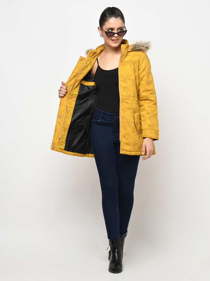 A woman wearing a Mustard Puffer jacket with a high neck, hood, zipper closure and pocket in hand designed for casual winter layering and comfort.