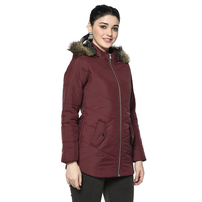 A left pose of a woman wearing a Maroon pufferjacket with a high neck, hood, zipper closure and pocket in hand designed for casual winter layering and comfort.