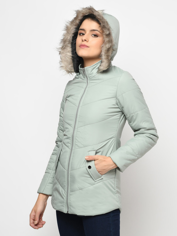 A left pose of a woman wearing a Mint Green pufferjacket with a high neck, hood, zipper closure and pocket in hand designed for casual winter layering and comfort.