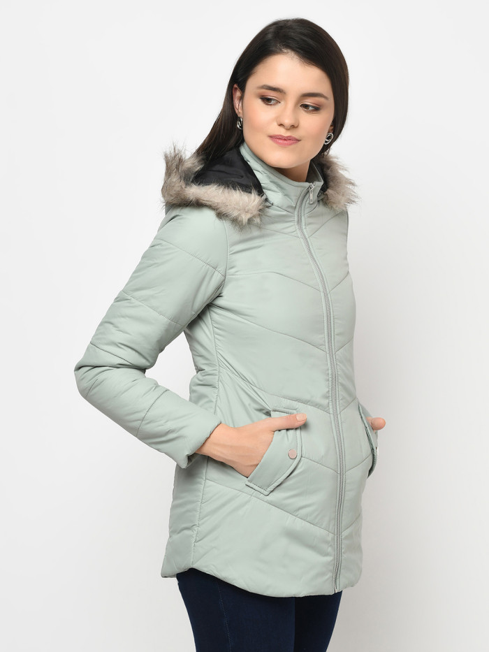 A left pose of a woman wearing a Mint Green pufferjacket with a high neck, hood, zipper closure and pocket in hand designed for casual winter layering and comfort.