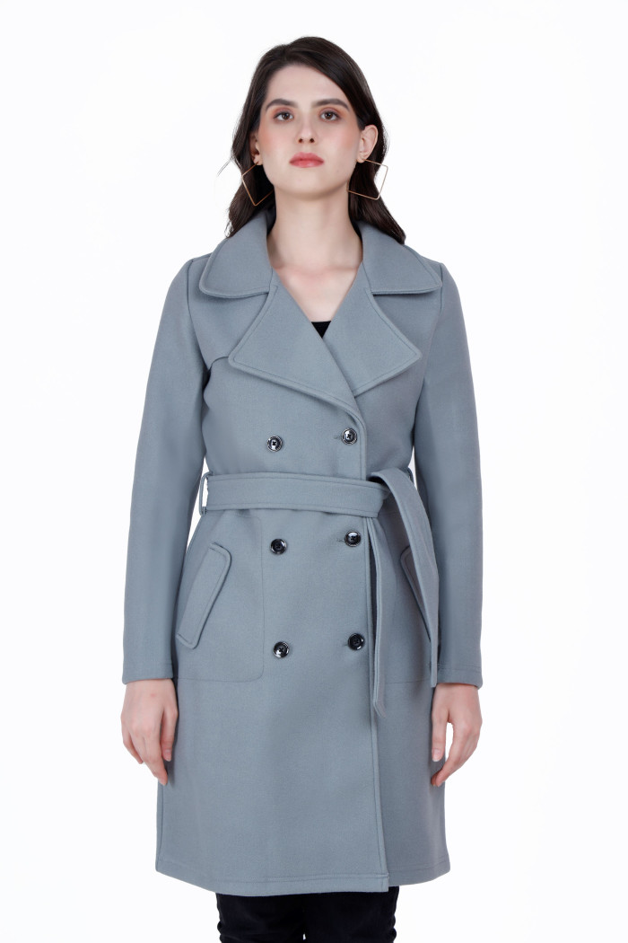 A woman wearing a Grey Long Coat with lapel collar, belt, button closure and pocket in hand designed for formal and casual winter layering and comfort.